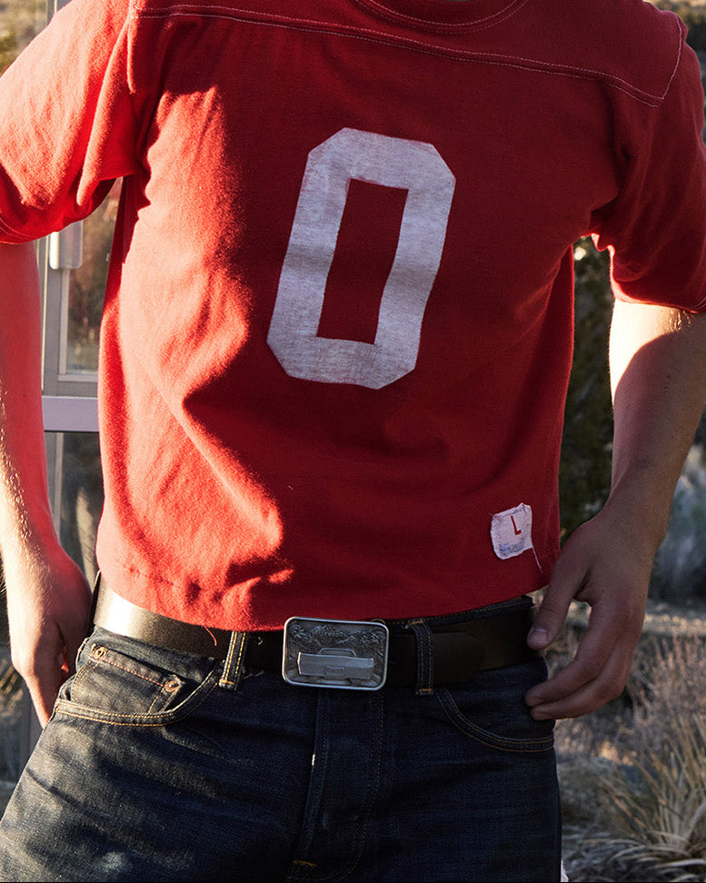 man wearing a red shirt with a number '0' in a desert setting with a phone booth. Wearing the Caballero Hollywood buckle and black classic caballero belt