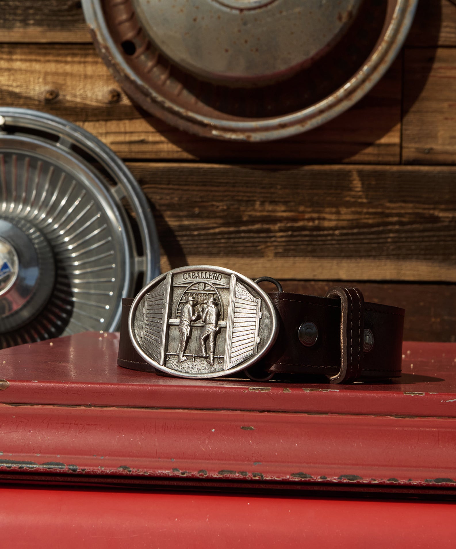 Caballero Bar Belt buckle and caballero brown stitched belt on a red table 